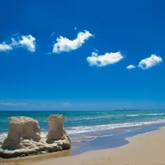 Spiagge libere Sicilia: rocce scolpite dal mare e sabbia dorata sotto un cielo azzurro con nuvole bianche.