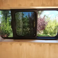 Fenêtre de fourgon aménagé, prête pour le contrôle technique. Vue sur un jardin verdoyant et fleuri.