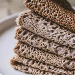 Pile de crêpes et de galettes, certaines roulées, d'autres pliées, avec une texture alvéolée. Un délice qui rappelle le goût de l'andouille.