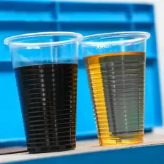 Dwa kubki z płynami: ciemny olej i jasny olej, porównanie stanu po użyciu i nowego. Może to być test filtra oleju skrzyni biegów.