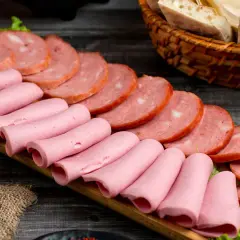 Na desce ułożone są różowe parówki i plastry wędliny. Zastanawiasz się, jakie wędliny są najzdrowsze?