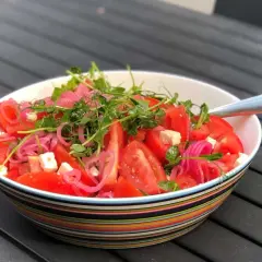 En skål med en färgglad tomatsallad med fetaost, rödlök och groddar. En god sallad till maten som ser fräsch och inbjudande ut.