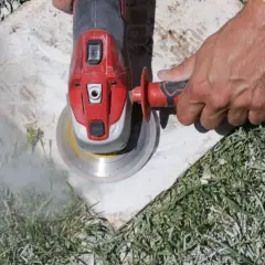 Main d'un ouvrier utilisant une meuleuse pour enlever ciment colle sous carrelage. Nuage de poussière.