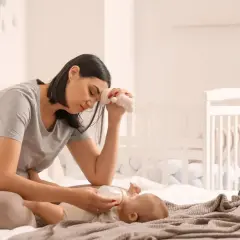 Madre esausta che allatta il neonato, con un peluche in mano, simbolo della sua lotta contro la depressione post partum.