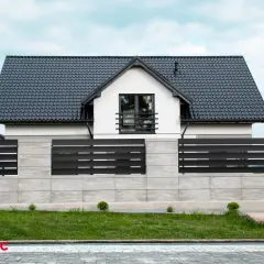Nowoczesne projektowanie ogrodzenia z betonowych bloczków i czarnych paneli, otaczające biały dom z czarnym dachem.