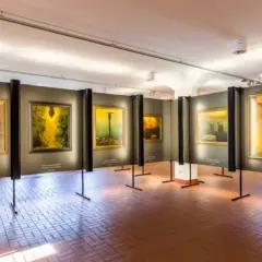 Wystawa obrazów Beksińskiego w galerii, z widocznymi dziełami w żółtych i brązowych barwach.