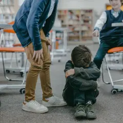 Chłopiec siedzi na podłodze, skulony, podczas gdy inni chłopcy stoją nad nim.