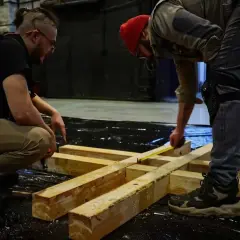 Dwóch mężczyzn planuje, jak połączyć belki drewniane, mierząc je taśmą.