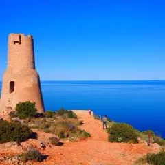 Torre defensiva en la costa, un lugar ideal que ver en Gata, con el mar azul de fondo y visitantes disfrutando del paisaje.