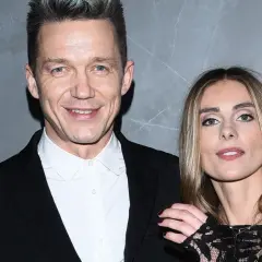 Katarzyna Zawadzka i jej mąż, uśmiechnięci, pozują do zdjęcia na tle szarej ściany.
