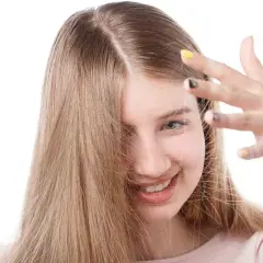 Chica sonriente con cabello rubio que se toca la frente, buscando cómo quitar la electricidad del pelo.