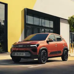 Pomarańczowa Dacia Spring na tle nowoczesnego budynku. Sprawdź atrakcyjną dacia spring cena i wybierz swój wymarzony samochód elektryczny.