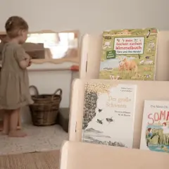 Ein kleines Mädchen in einer Montessori Kita entdeckt Bücher über Tiere und den Sommer.