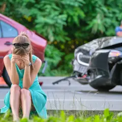 Mujer sentada en el suelo, con las manos en la cara, tras un accidente de coche. Parece que va a soñar con accidente de coche.
