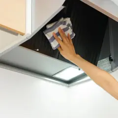 Mano limpiando campana extractora por fuera con un paño a rayas.