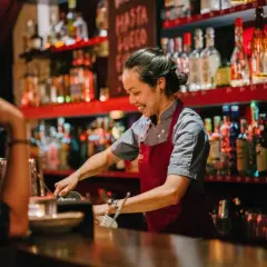 Uśmiechnięta barmanka w Gdańsku przygotowuje drinka. Zastanawiasz się, ile zarabia barman w Gdańsku?