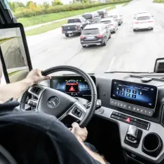 Fahrer im LKW-Cockpit mit Blick auf die Straße und ein Display, das die allgemeine Sicherheitsvorschrift anzeigt.