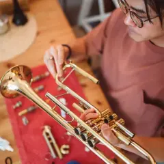 Un homme nettoie son instrument cuivre, une trompette, sur une table en bois.