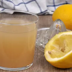 Verre de jus de citron frais, citrons coupés et presse-agrumes. Découvrez les jus de citron bienfaits pour la santé.