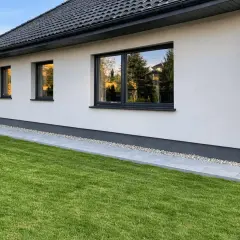 Nowy dom z zadbanym ogrodem. Wokół domu biegnie ścieżka z płyt i kamieni, tworząc estetyczną opaskę wokół domu.