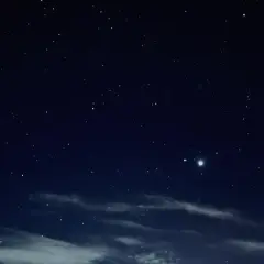 Nocne niebo pełne gwiazd, z widocznymi chmurami i dwoma jasnymi punktami, być może planetami.
