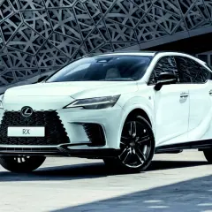 Biały Lexus RX 500h z czarnymi felgami stoi przed nowoczesnym budynkiem o geometrycznej fasadzie.