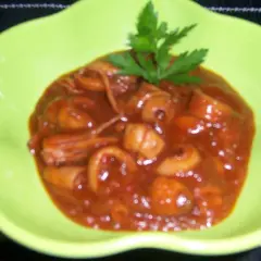 Calamares a la riojana en un plato verde brillante, cubiertos de una salsa roja y decorados con perejil.