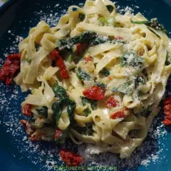Pyszny makaron tagliatelle ze szpinakiem i suszonymi pomidorami, posypany parmezanem. Idealny na szybki obiad.