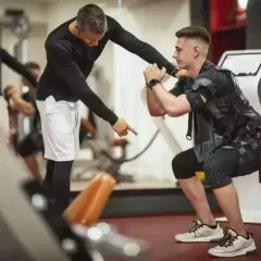Trener instruuje mężczyznę w kamizelce EMS podczas ćwiczeń w siłowni.