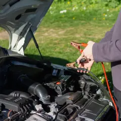 Ręce trzymające kable rozruchowe przy akumulatorze. Czy można odpalic auto na wlaczonym prostowniku?