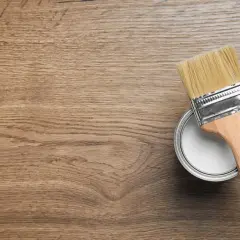 Pennello e barattolo di vernice bianca pronti per colorare legno su una superficie di legno grezzo.