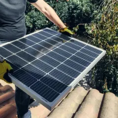 Person med gula handskar håller solpanel på taket. Undrar du vad kostar batteri till solceller?