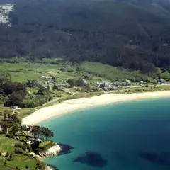 Vista aérea de la playa de Area, Viveiro, con casas dispersas entre verdes colinas y el mar turquesa.