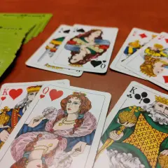 Król i dama tego samego koloru, serce i karo, leżą obok siebie. Zielona talia kart czeka na grę.