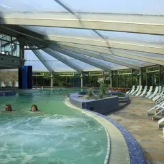 Entspannen in der Therme NRW: Zwei Frauen schwimmen im warmen Wasser unter einem Glasdach, Liegen laden zum Verweilen ein.