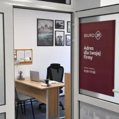 Widok biura rachunkowego z biurkiem, laptopem i tablicą ogłoszeń. Na drzwiach widnieje logo i godziny otwarcia.