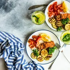 Dwa talerze z łososiem, grillowaną cukinią i pomidorami. Idealne danie na dieta niskowęglowodanowa.