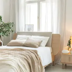 Jak urządzić przytulną sypialnię: łóżko z beżowym zagłówkiem, miękki koc, lampka nocna i rośliny tworzą ciepłą atmosferę.