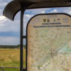 Mapa informuje o ścieżce rowerowej trasą dawnej kolejki wąskotorowej. Obok stoi rower.