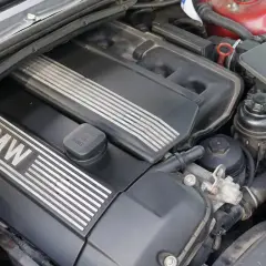 Silnik BMW e46, widok z góry. Czarna pokrywa silnika z napisem BMW i metalowymi wstawkami. Widać też elementy układu dolotowego i zbiorniczek płynu.