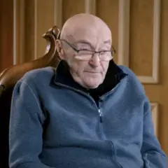 Phil Collins, zmagający się z chorobą, siedzi w fotelu, ubrany w niebieski polar.