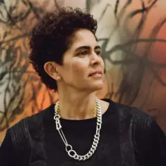 A striking portrait of artist Julie Mehretu, her gaze thoughtful, set against a vibrant, abstract background that echoes her dynamic style.