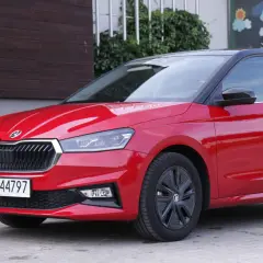 Czerwona Skoda Fabia 4 z czarnym dachem i felgami stoi przed budynkiem z drewnianą elewacją.