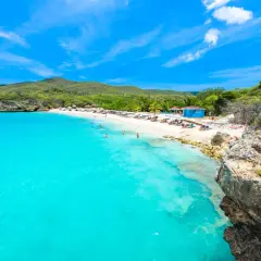Traumhafter Curacao Beach mit türkisblauem Wasser, weißem Sand, Liegestühlen und Menschen, die schwimmen und sich sonnen.