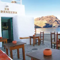 Mesas y sillas de madera en la terraza de "La Bodeguilla", con vistas al mar y a las barcas las negras.