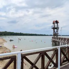 Plaża z ludźmi, pomost z wieżą ratowniczą i jezioro w Pogorii.
