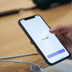 Dłoń trzyma iPhone'a, na ekranie którego wyświetla się komunikat "Face ID". Wygląda na to, że Face ID nie działa.