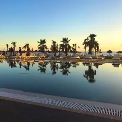 Zachód słońca nad basenem w Blumare Resort. Palmy i leżaki odbijają się w spokojnej wodzie.
