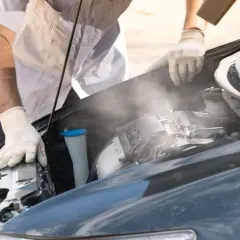Para wylatuje z gorącego silnika po jeździe. Mechanik w rękawiczkach sprawdza auto.
