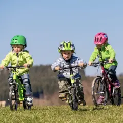 Trójka dzieci w kaskach uczy się jeździć na rowerze po trawiastym wzgórzu. Radość i pierwsze sukcesy w nauce jazdy na rowerze.